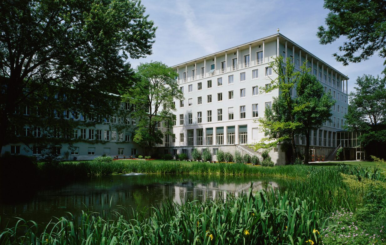 Il quartier generale di Allianz a Monaco di Baviera, in Germania. Una costruzione bianca di 5 piani inserita in un contesto verde di alberi, piante e un laghetto davanti